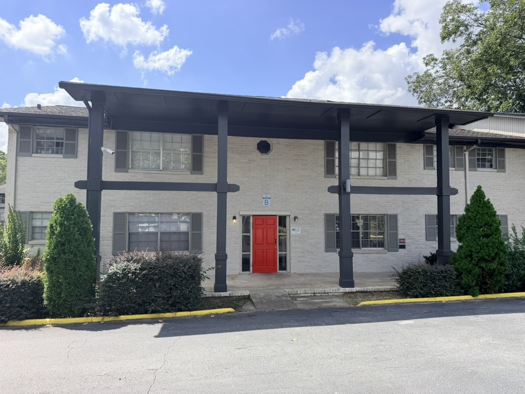 Front exterior of Building B with white brick, dark columns, and a red entry door