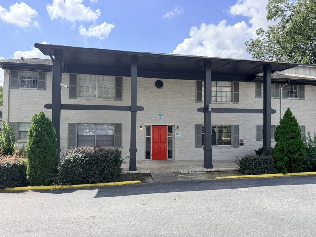 The Gillem Apartments exterior with white brick, shaded walkways, landscaping, and a red entry door